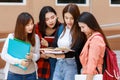 Group of four college student girls holding books standing and reading together. Learning and friendship of teens close friend