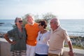 Group of four mature people having fun and talking together at the beach - pensioners seniors smiling and laughing with the sea at Royalty Free Stock Photo