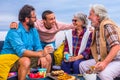 Group of four people of all ages together at home in the balcony laughng and having fun and eating food like fruit and cookies - Royalty Free Stock Photo