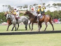 Group four polo players and horses compete for the ball with mallets raised