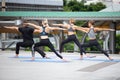 group of four sport people doing yoga on mat in urban city outdoors. fitness man and women exercise stretching arm together .