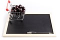 Group of fresh red cherries in a small shopping cart next to a pen on a black chalkboard Royalty Free Stock Photo