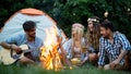 Group of friends camping.They are sitting around camp fire, playing guitar Royalty Free Stock Photo