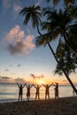 Group of friends celebrates sunset, standing with arms raised on Caribbean beach