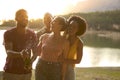 Group Of Friends Celebrating Outdoors By Lake Opening And Spraying Bottle Of Champagne