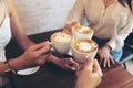 Group of friends cheers with latae cup in cafe bar with phone on table sitting intdoor at cafe - Young girl group having fun