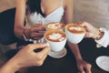 Group of friends cheers with latae cup in cafe bar with phone on table sitting intdoor at cafe - Young girl group having fun