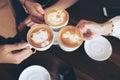 Group of friends cheers with latae cup in cafe bar with phone on table sitting intdoor at cafe - Young girl group having fun