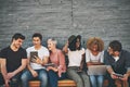 Group of friends on digital devices and social media sitting together while smiling and talking. Technology obsessed