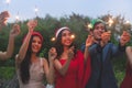 Group of friends enjoying with sparklers in the party. Selective focus on face of woman in red dress Royalty Free Stock Photo