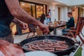 A group of friends and family barbecue together in the evening on the terrace in front of a large modern house