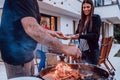 A group of friends and family barbecue together in the evening on the terrace in front of a large modern house