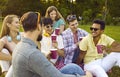 Group of friends gather together in summer park and talk on picnic with paper cups of coffee or tea. Royalty Free Stock Photo