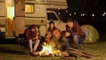 Group of friends gathered around camp fire in a cold night of autumn