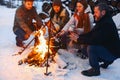 Group of friends gathering around bonfire in backyard, drinking tea and warming hands Royalty Free Stock Photo