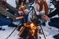 Group of friends gathering around bonfire in backyard, drinking tea and warming hands Royalty Free Stock Photo