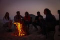 Group of friends gathering around bonfire on beach in evening. Camping season