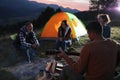 Group of friends gathering around bonfire at camping site in evening Royalty Free Stock Photo