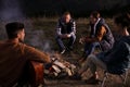 Group of friends gathering around bonfire at camping site in evening Royalty Free Stock Photo