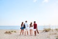 Group of friends going to sandy beach at sunset. Young men and women walking to the shore to relax near sea and play Royalty Free Stock Photo