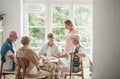 Group of friends with helpful carer sitting together at the table at nursing home dining room