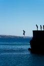 Group of friends jumping into mediterranean sea from rock cliff