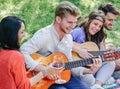 Group of friends playing guitars and laughing while drinking red wine sitting on grass in a park outdoor Royalty Free Stock Photo