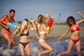 Group of friends playing with water pistols in water at beach. Young adults on summer vacation together having water gun battle. Royalty Free Stock Photo