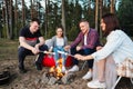 A group of friends relax in a forest camp. Men and women prepare a marshmallow on a bonfire. A party in nature. Royalty Free Stock Photo