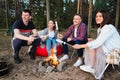 A group of friends relax in a forest camp. Men and women prepare a marshmallow on a bonfire. A party in nature. Royalty Free Stock Photo