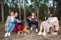 A group of friends relax in a forest camp. Men and women prepare a marshmallow on a bonfire. A party in nature. Royalty Free Stock Photo