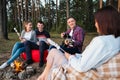 A group of friends relax in a forest camp. Men and women prepare a marshmallow on a bonfire. A party in nature. Royalty Free Stock Photo