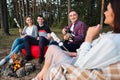 A group of friends relax in a forest camp. Men and women prepare a marshmallow on a bonfire. A party in nature. Royalty Free Stock Photo