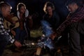 Group of friends roasting marshmallows on bonfire at camping site in evening Royalty Free Stock Photo