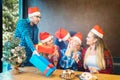 Group of friends with Santa hats celebrating Christmas by sharing gifts and drinking champagne at home dinner Royalty Free Stock Photo