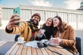 group of friends sitting on a bar terrace or restaurant having fun taking a selfie portrait with a smartphone outdoors Royalty Free Stock Photo