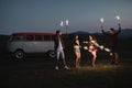 A group of friends with sparklers standing outdoors at dusk.