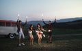 A group of friends with sparklers standing outdoors at dusk.