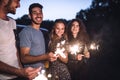 A group of friends with sparklers standing outdoors at dusk.