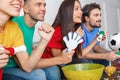 Group of friends sport fans watching match in colorful shirts holding noisemakers close-up Royalty Free Stock Photo