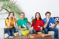 Group of friends sport fans watching match in colorful shirts holding noisemakers Royalty Free Stock Photo