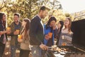 Group of friends stand at a barbecue, one cooking at grill Royalty Free Stock Photo