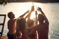 A group of friends in swimsuit is enjoying drink and the sunset on the bank of the river. Summer, river, vacation