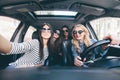 Group of girls having fun in the car and taking selfies with camera on road trip Royalty Free Stock Photo
