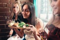 Group of girls having lunch in fashionable restaurant. Smiling young woman enjoying the smell of delicious salad served Royalty Free Stock Photo