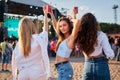 Group of girls toast drinks at beach music festival. Sunlit scene of fun, dance near stage. Summer event vibes with