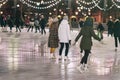 Group of girs skating back to us. Girlfriends ice skating in city park, snowy evening. Healthy outdoor winter activity