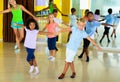 Group of children practicing vigorous jive movements in dance class with female coach