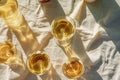 Group of glasses with white wine on a table with beige fabric linen fold. Minimalist trendy style. Gentle sunlight, caustic light