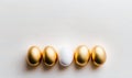 a group of golden and white eggs on a white surface with one white egg in the middle of the row of the eggs, and the third white Royalty Free Stock Photo